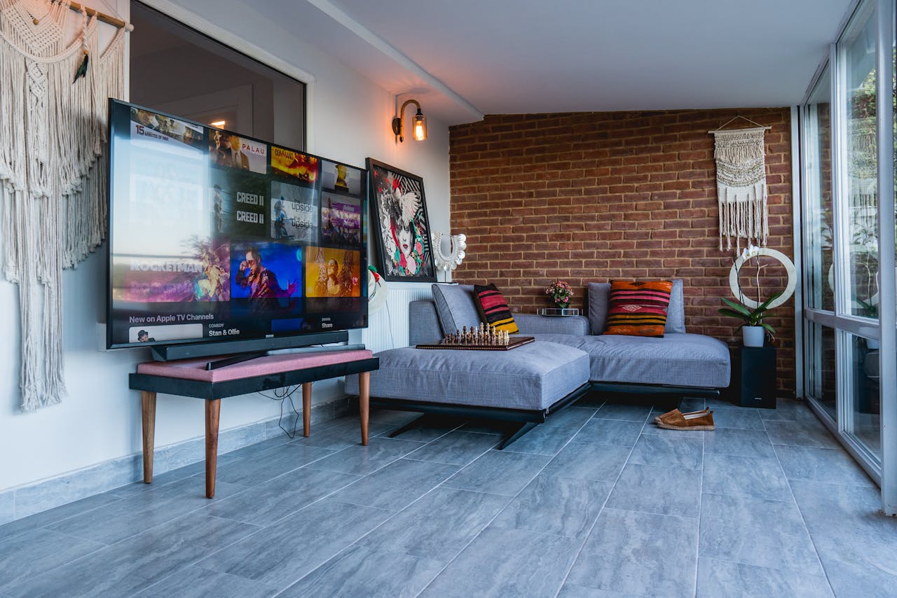 Chic modern living space featuring a large TV and comfortable couch against brick wall.